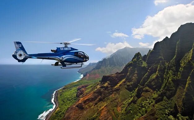 Helicopter flying over rugged terrain of Kauai and ocean