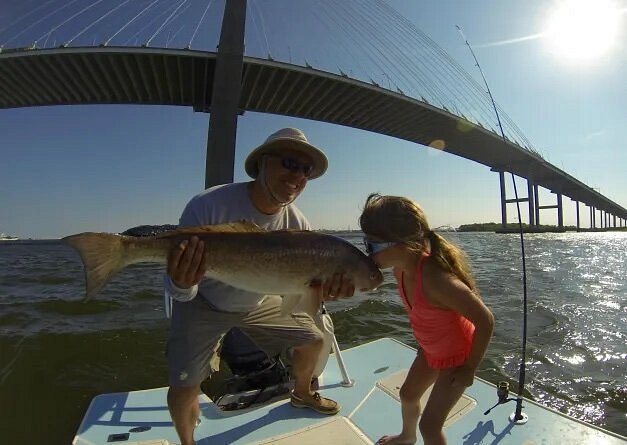 Child kissing fish held up by adult on a boat