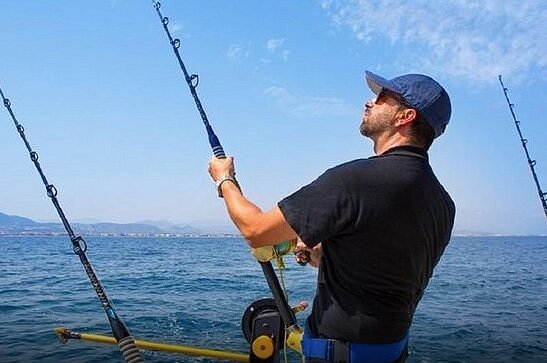 Adult holding fishing pole into ocean on boat 