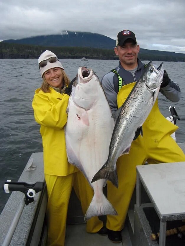 Two people in yellow fishing gear holding large fish