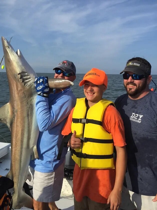 Adult holding caught shark with two people next to him on boat