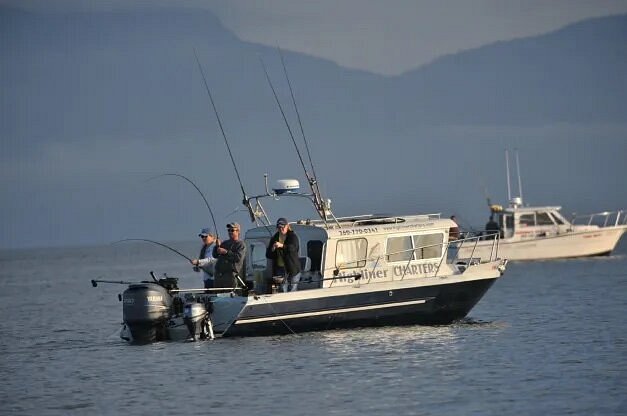 Three people fishing from boat with another boat in background