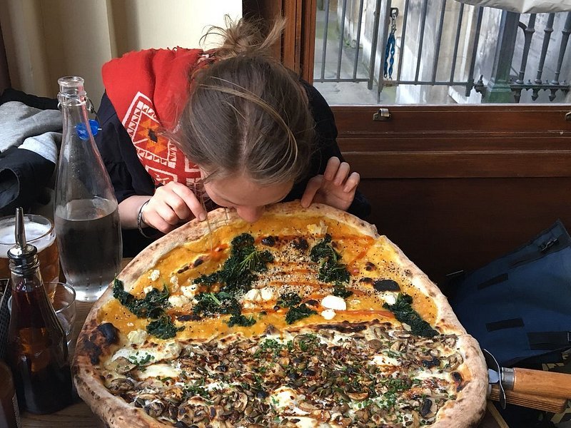 A girl eating a huge pizza at Homeslice restaurant in London