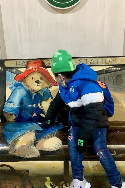 A boy sitting next to the Paddington Bear chair in London