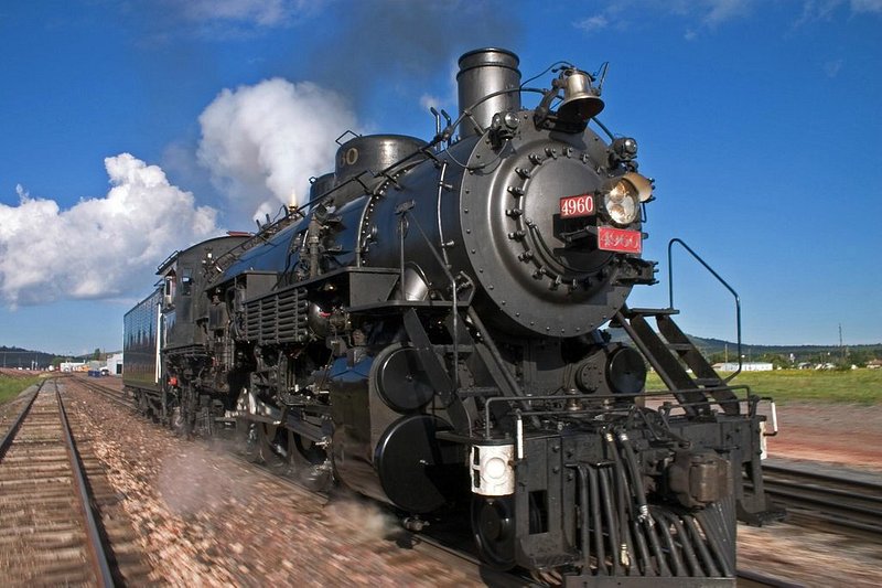 A large black steam train moving forward with bright blue sky in the background