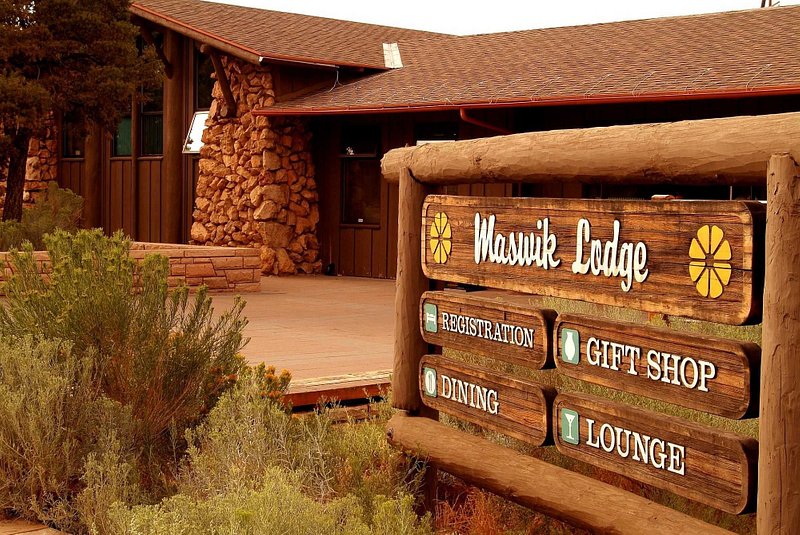 A 45-degree angle looking at the wooden brown sign announcing Maswik Lodge and its registration, lounge, dining, and gift shop
