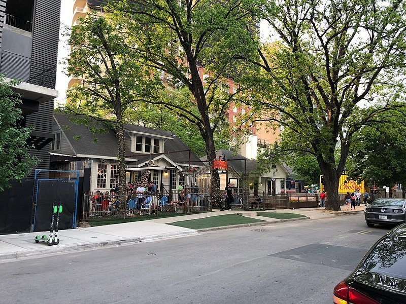 Full, leafy green trees shade a street with a bustling patio