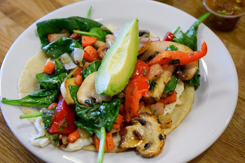 Two tacos filled with red bell pepper, spinach, avocado, mushrooms and tomatoes