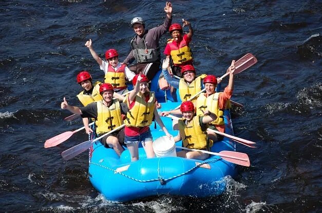 People holding oars in blue raft and waving 