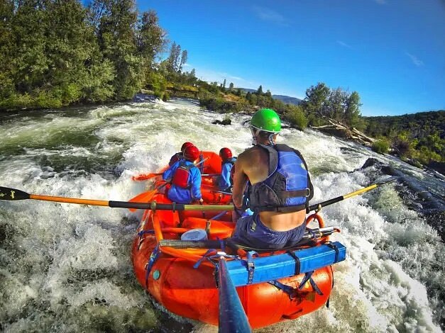 View from back of people on red raft going over rapids