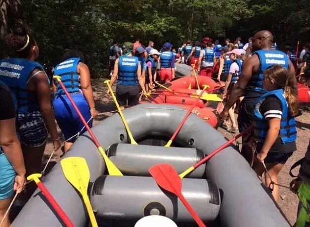 Dozens of people carrying rafts on ground