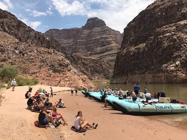 Raft boats docked within canyon, with people sitting on ground