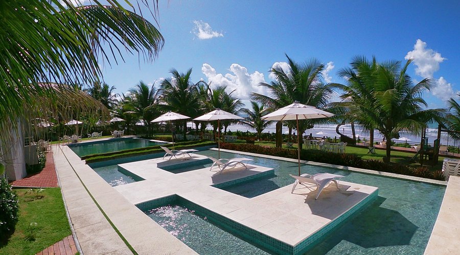 Área de lazer com piscina, espreguiçadeiras e guarda sol. 