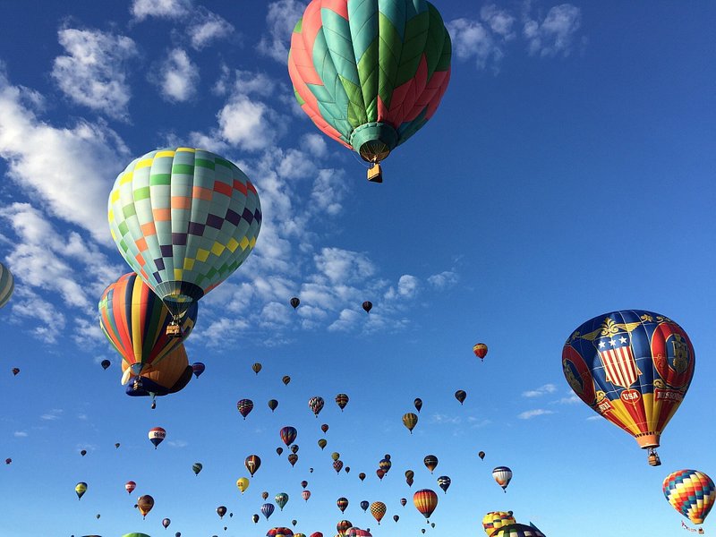 Dozens of colorful hot air balloons lift into a blue sky