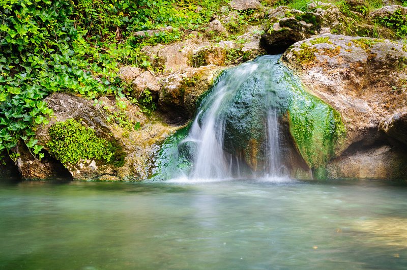 A waterfall flows off a moss-covered boulder into hot springs