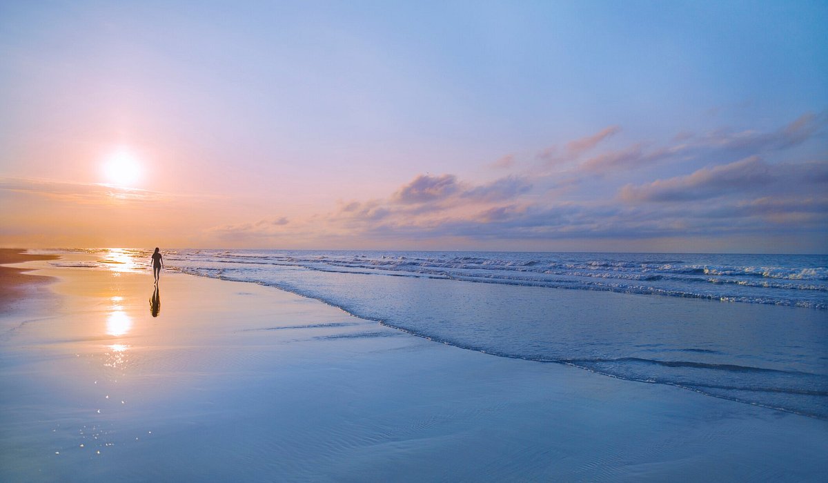 Person walking along shoreline at beach next to ocean at sunrise