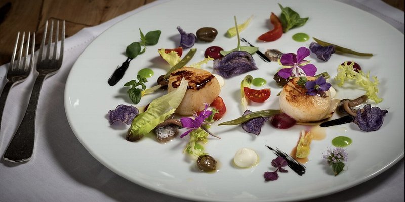 A colorful dish of seared scallops beautifully plated with flowers
