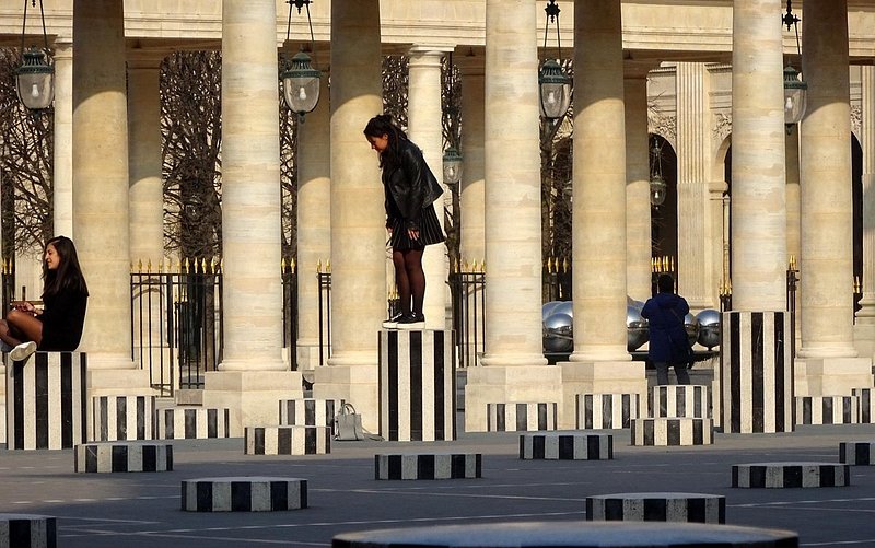 A woman standing on top of a column as part of Les Colonnes de Buren in Paris