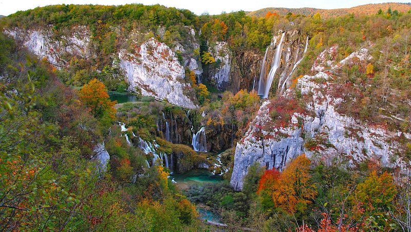 Several huge waterfalls surrounded by rock and fall foliage trees 