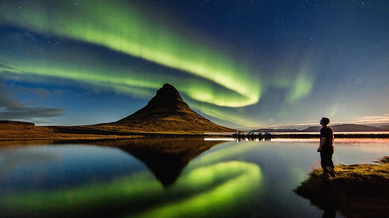 Silhueta a observar uma aurora boreal sobre Kirkjufell, na Islândia