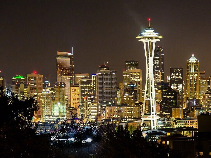 The Space Needle, a spaceship-shaped platform on top of three warped pillar legs, is lit up in the night with the Seattle skyline behind it
