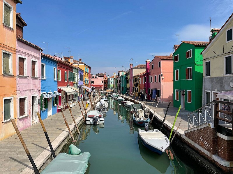 A canal lined filled with small boats and lined with colorful pink, orange, blue, and green buildings