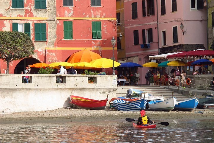 A kayaker paddles up toward a shore with colorful boats and colorful buildings