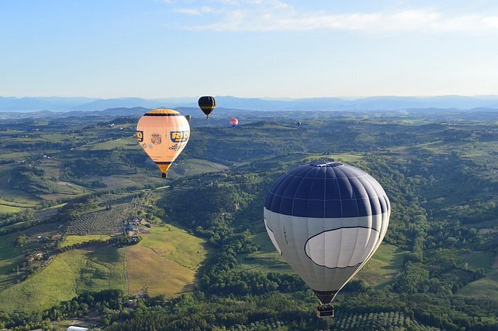 Six hot air balloons at varying distances over a rolling green hillside