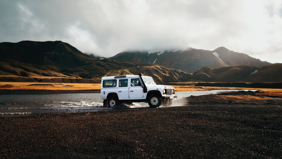 A white SUV is parked amongst snow-capped mountains