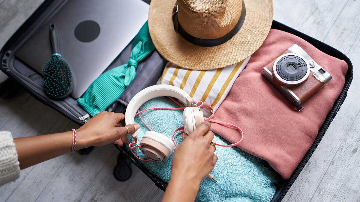 Woman organizing open luggage filled with items ready to go on vacation.
