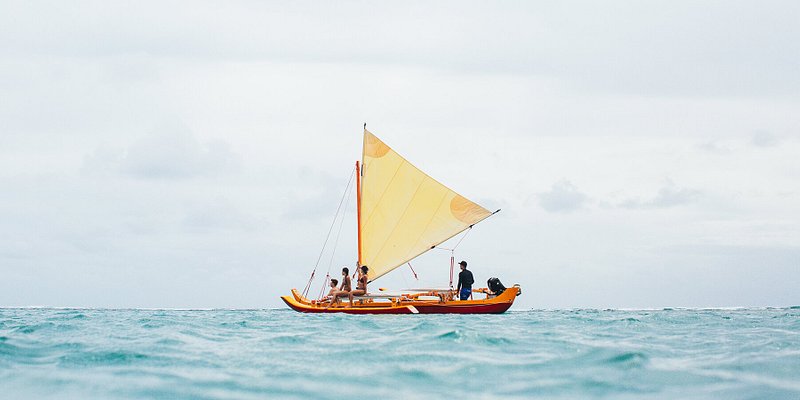 Небольшая парусная лодка плывет по кристально голубым водам Кахала-Бич на Гавайях