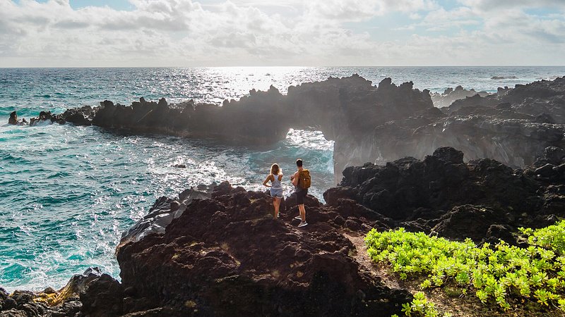 A couple takes in the vista view atop a rocky cliff at the Waiʻānapanapa State Park in Hawaii