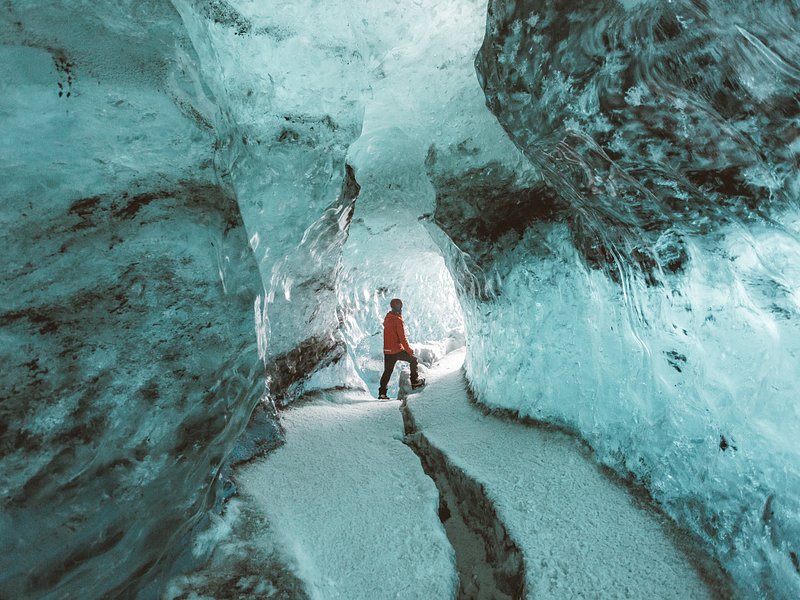 A man in orange padded jacket exploring a ice cave in Iceland