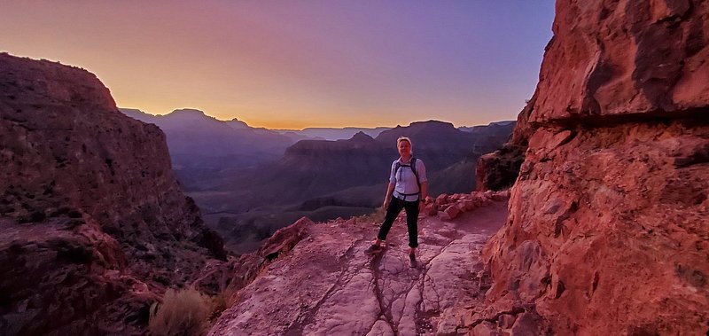 Magenta and blue light paints the canyon walls as a person stands on a trail