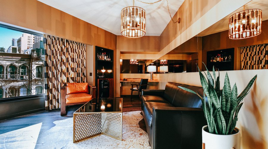 Roxy Hotel New York | Deluxe One Bedroom Suite Living Area with expansive downtown views, natural light, full size bar, work desk, record player with curated vinyl selection.