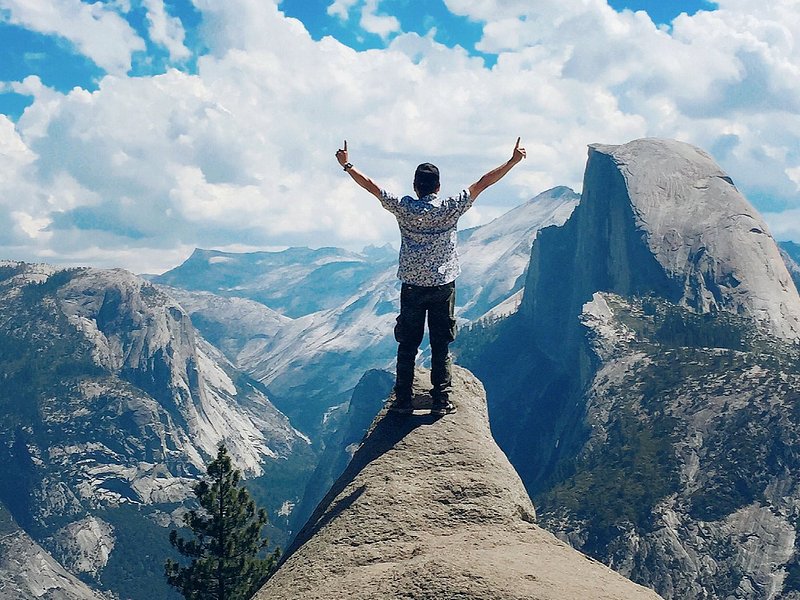 A person stands with their arms in the air, the granite face of Half Dome looming large in the near distance