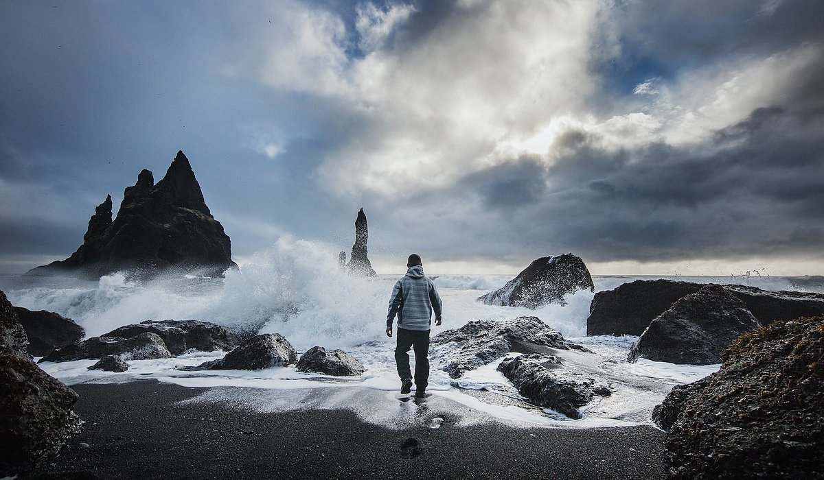 Um homem na praia de areia preta Reynisfjara, Islândia
