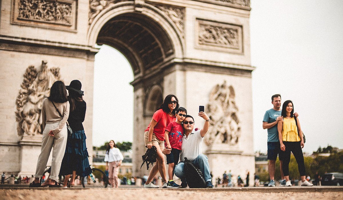 A family taking a selfie in front of the Arc de Triomphe de l'Étoile in Paris, France