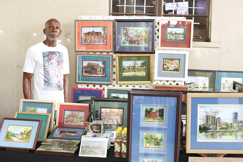 Artist standing next to booth with dozens of framed art pieces