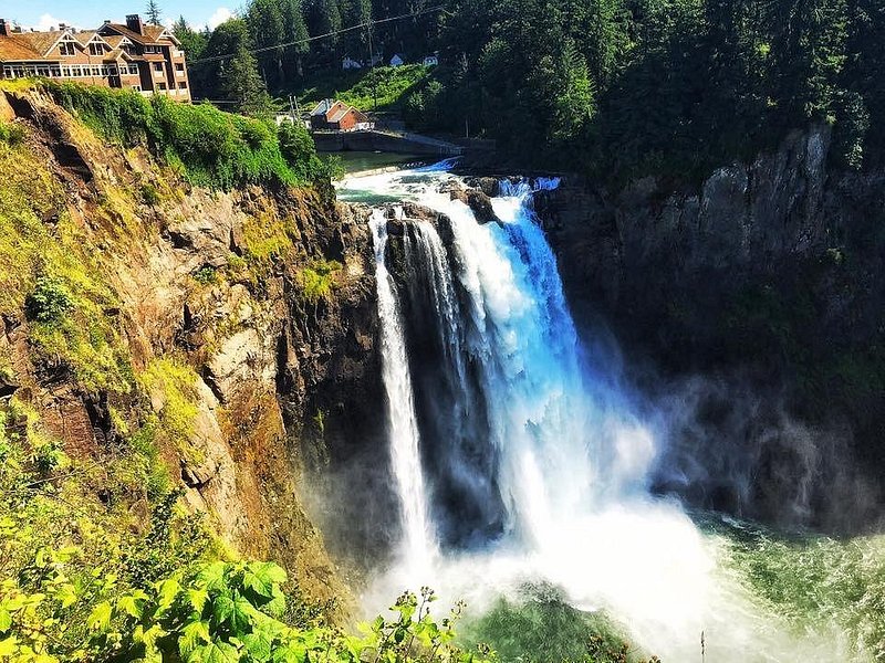 Snoqualmie Falls plummets off a cliffside, with the Salish Lodge building at the edge of its lip to the top left