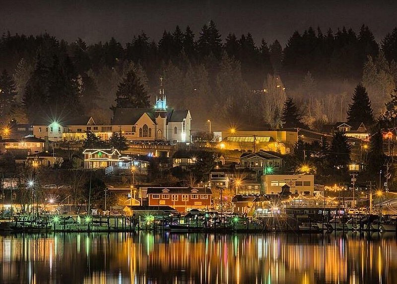 A night scene of Poulsbo's downtown businesses glowing in the dark and reflecting in Liberty Bay