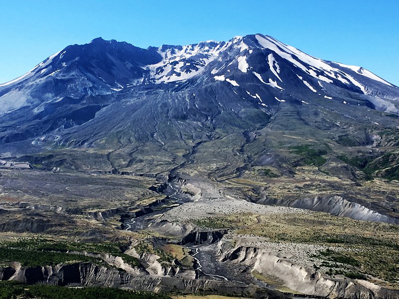 The wide bowl-shaped crater of Mount St. Helens, dotted with snow, with its stripped-bare landscape spreading beneath
