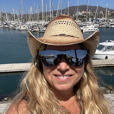 Woman in cowboy hat and sunglasses smiling in front of marina