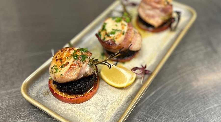 Scallops wrapped in Streaky Bacon, skewered with Rosemary and served on Baked Apple and Black Pudding.  Drizzled with Garlic Butter