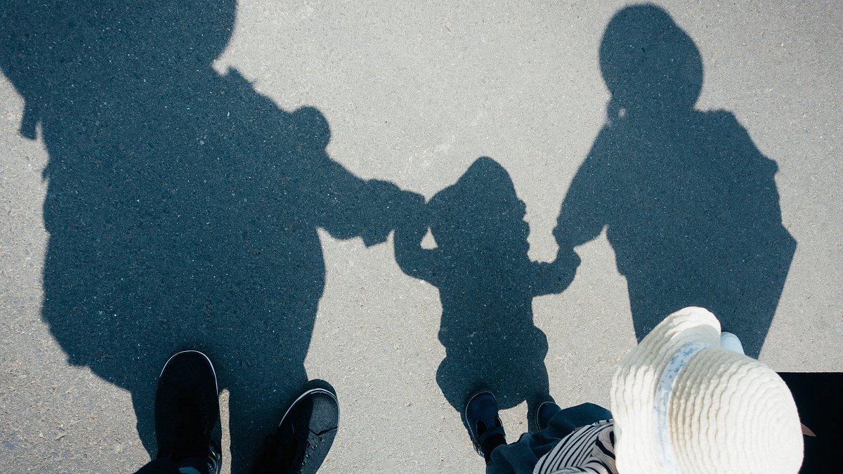 Shadow on gravel path of a family of three holding hands walking outdoors on a sunny day 