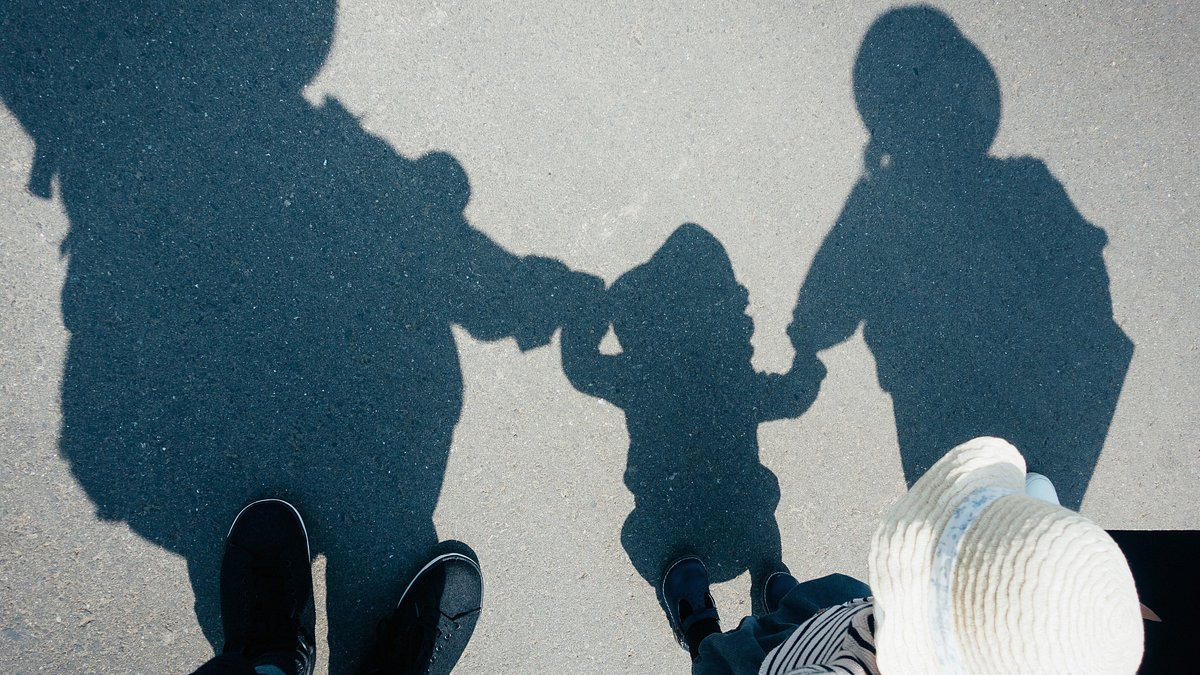 Shadow on gravel path of a family of three holding hands walking outdoors on a sunny day