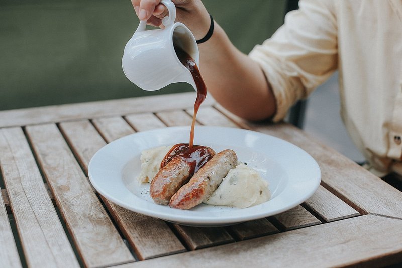 A woman pouring gravy over a plate of bangers and mash from Mother Mash in London