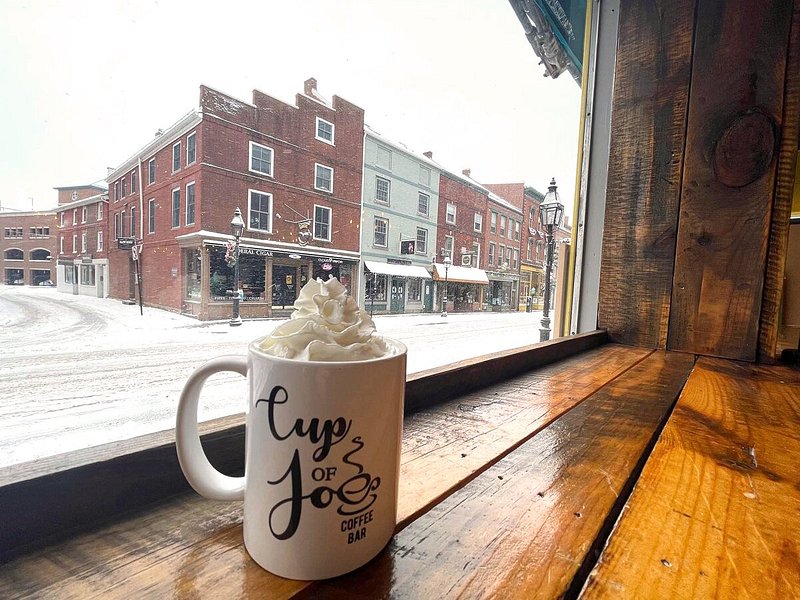 Mug with "Cup of Joe" written on it next to window overlooking snowy street