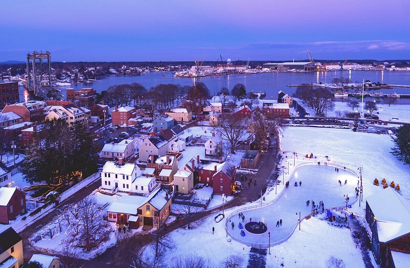 An aerial view of snow-surrounded skating rink, surrounding buildings, and body of water at night