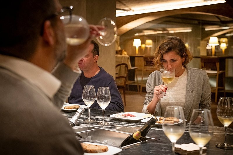 People sitting at table during wine tasting, with one person smelling into glass of wine and another drinking from a glass